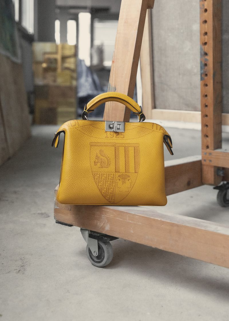 Designer yellow leather Fendi handbag featuring a crest design on a wooden dolly inside of an artist's studio; high-fashion editorial.