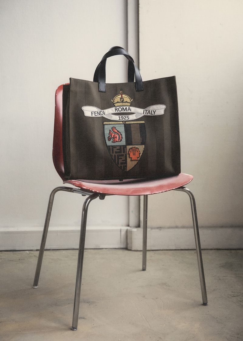 Fendi Roma Italy striped logo tote bag displayed on a red chair in a brightly lit interior, product shot for fashion.