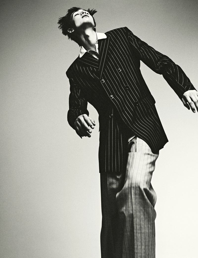 A man in a pinstripe suit strikes a dynamic pose against a neutral backdrop, showcasing a fashion-forward and artistic black-and-white photograph.