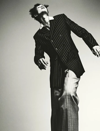 A man in a pinstripe suit strikes a dynamic pose against a neutral backdrop, showcasing a fashion-forward and artistic black-and-white photograph.