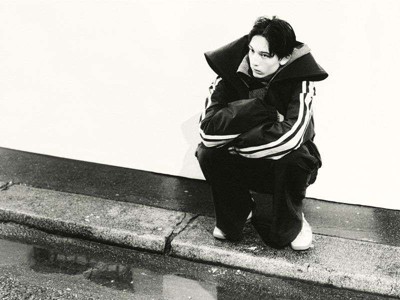 Monochrome image of a crouched person wearing a jacket with stripes, set against a bright white backdrop with a wet foreground.