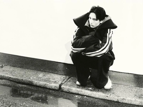 Monochrome image of a crouched person wearing a jacket with stripes, set against a bright white backdrop with a wet foreground.