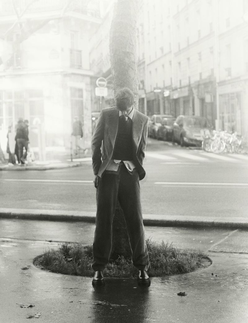Model wearing a blazer and trousers standing by a tree on a city street in a monochrome editorial photograph