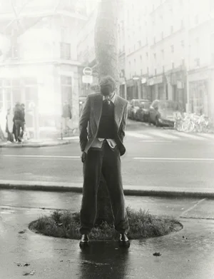 Model wearing a blazer and trousers standing by a tree on a city street in a monochrome editorial photograph