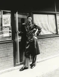 Black man wearing a long dark trench coat posing in a doorway for HERO Magazine captured by Sungmin Kim.