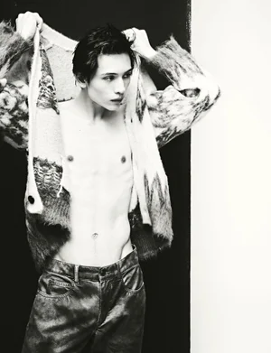 Black and white portrait of a male model putting on a patterned knit cardigan against a split dark and light background