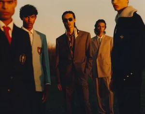 Group of male models in tailored blazers and suits standing outdoors during golden hour for HERO Magazine