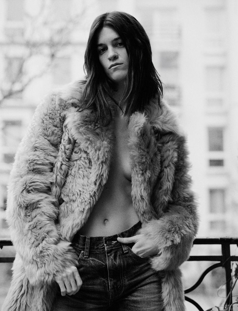 Suzanne Lindon wearing a textured fur coat and denim jeans posing outdoors on a balcony for Heroine Magazine.
