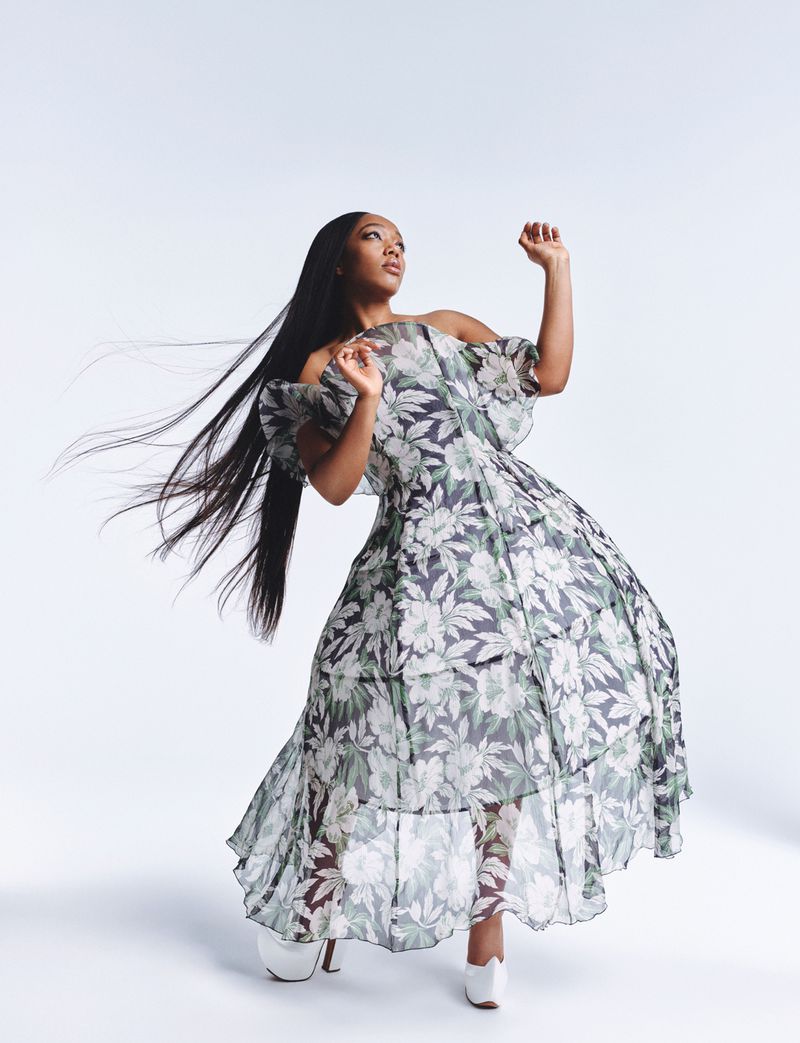 An adult female in a flowing floral dress with long hair posed against a clean white background.