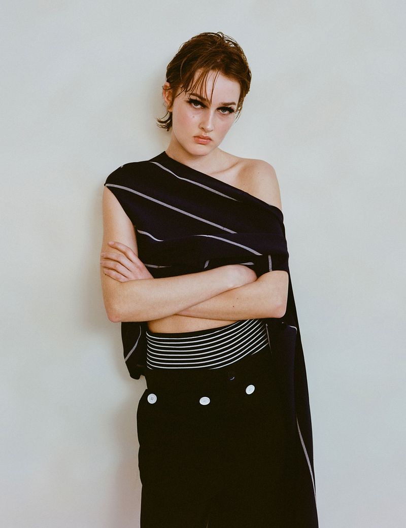 Striking portrait of a woman in a fashionable black and white striped outfit posing against a neutral background with her arms crossed.