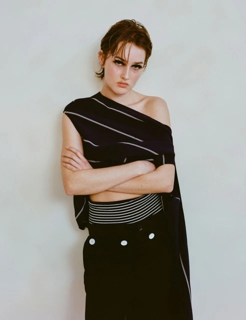Striking portrait of a woman in a fashionable black and white striped outfit posing against a neutral background with her arms crossed.