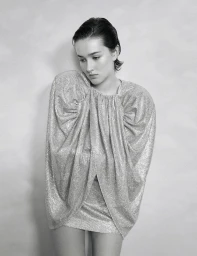 Model in silver metallic dress with voluminous shoulders posing against a neutral textured background