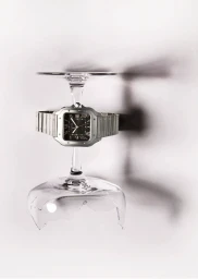 A silver square wristwatch balanced between two inverted glass stems against a plain white background.