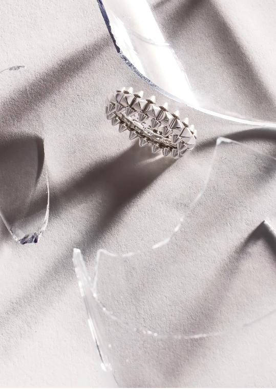 Close-up product shot of silver ring surrounded by shattered glass, emphasizing luxury jewelry with a modern, edgy aesthetic.