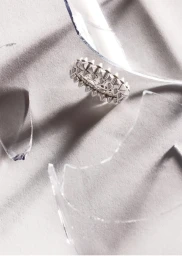 Silver studded ring viewed through shards of shattered glass on a textured grey background.