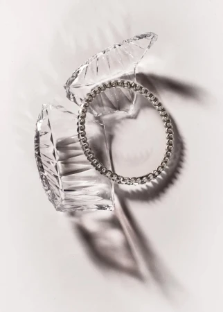 Elevated studio shot of a silver beaded bracelet resting inside an open crystal trinket box against a white backdrop with shadows.