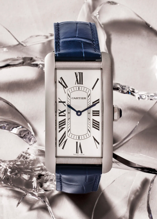 Wristwatch with a rectangular silver case and a blue leather strap is displayed against a background of cracked glass pieces.