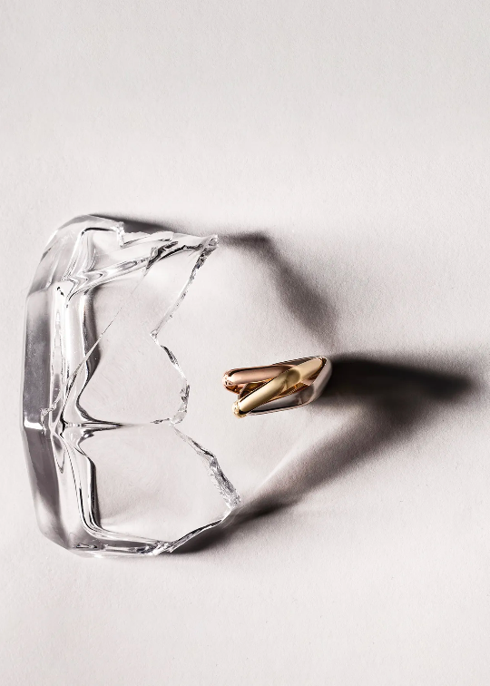 Close-up studio shot of a broken glass and two gold and white capsules, artfully arranged on a white surface with shadow play.