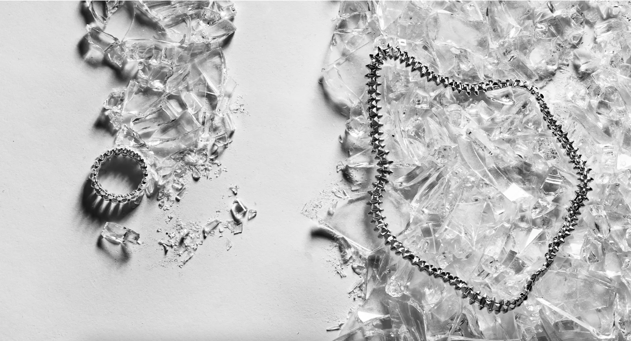 Jewelry flat lay: silver ring and necklace on shattered glass shards over a white background, product photography for fashion.