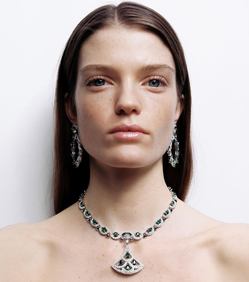 Close-up shot of an adult female model wearing a silver and green emerald necklace and earrings, against a plain white background.