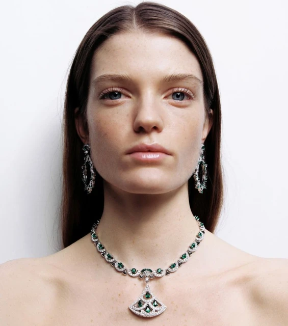Close-up shot of an adult female model wearing a silver and green emerald necklace and earrings, against a plain white background.