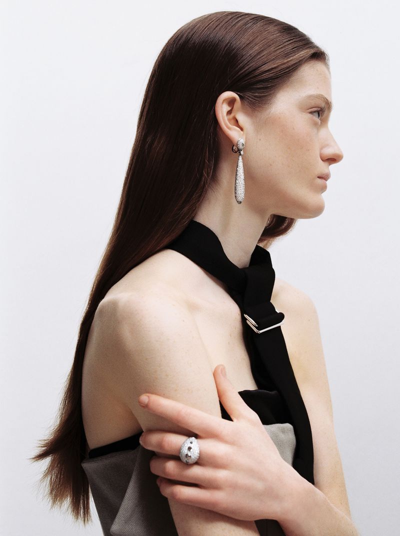 Profile portrait of a female model wearing diamond drop earrings and a statement ring against a white seamless background for Heroine Magazine.