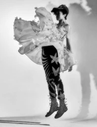 Model jumping mid-air wearing a patterned dress and cap against a bright white background