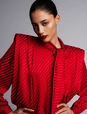 Model wearing a red structured blouse with padded shoulders against a plain grey studio backdrop.