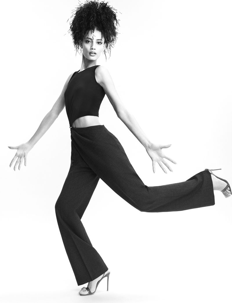 Monochrome fashion shot of a Black model in a dark jumpsuit and heels against a white background, full body pose, fashion editorial look.