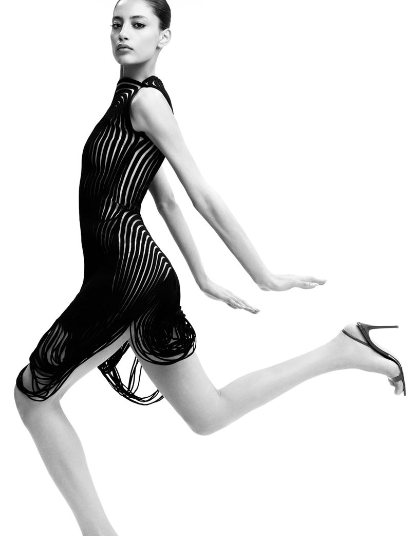 Woman in black dress and heels striking a dynamic pose against a white backdrop, showcasing fashion and design elements in a studio setting.