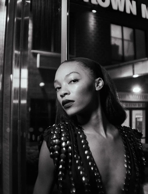 Monochrome portrait of a woman with dark lipstick and shoulder embellishments, posed in front of a dark building at night.