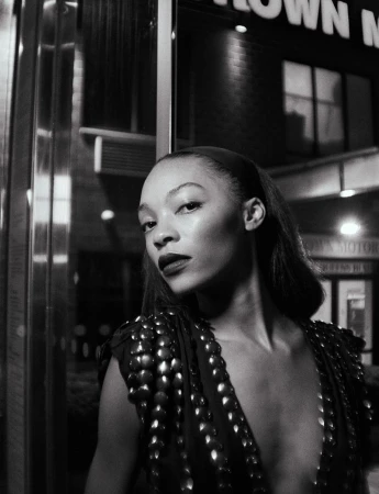 Monochrome portrait of a woman with dark lipstick and shoulder embellishments, posed in front of a dark building at night.
