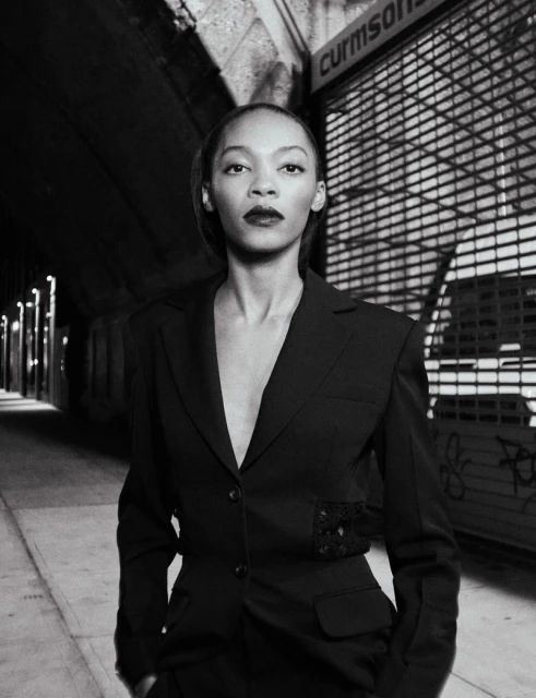 Black and white portrait of an adult woman in a dark business suit. The shot is set in an outdoor urban environment with concrete walls.