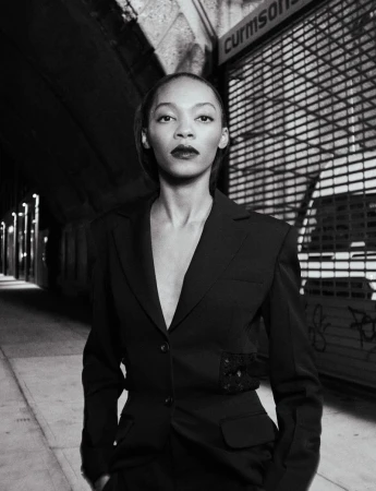 Black and white portrait of an adult woman in a dark business suit. The shot is set in an outdoor urban environment with concrete walls.