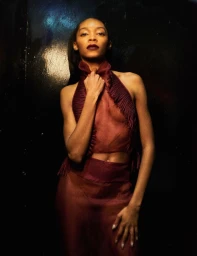 Model wearing a sheer burgundy halter top and matching skirt against a dark glossy background for Heroine Magazine.