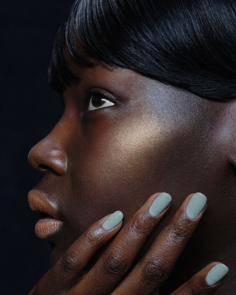 Close-up portrait of Ajok Daing with glossy sage green nail polish against a dark background for Chanel Beauty and Heroine Magazine.