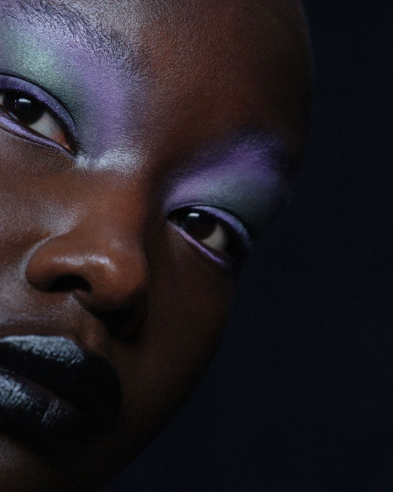 Close-up portrait of a dark-skinned adult woman with dramatic eye makeup, bold lipstick, and dark hair, captured in a studio setting.