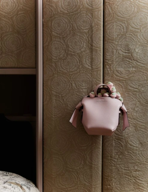 Designer handbag with floral accents against a textured wall. Close-up of a stylish accessory for fashion and personal style.