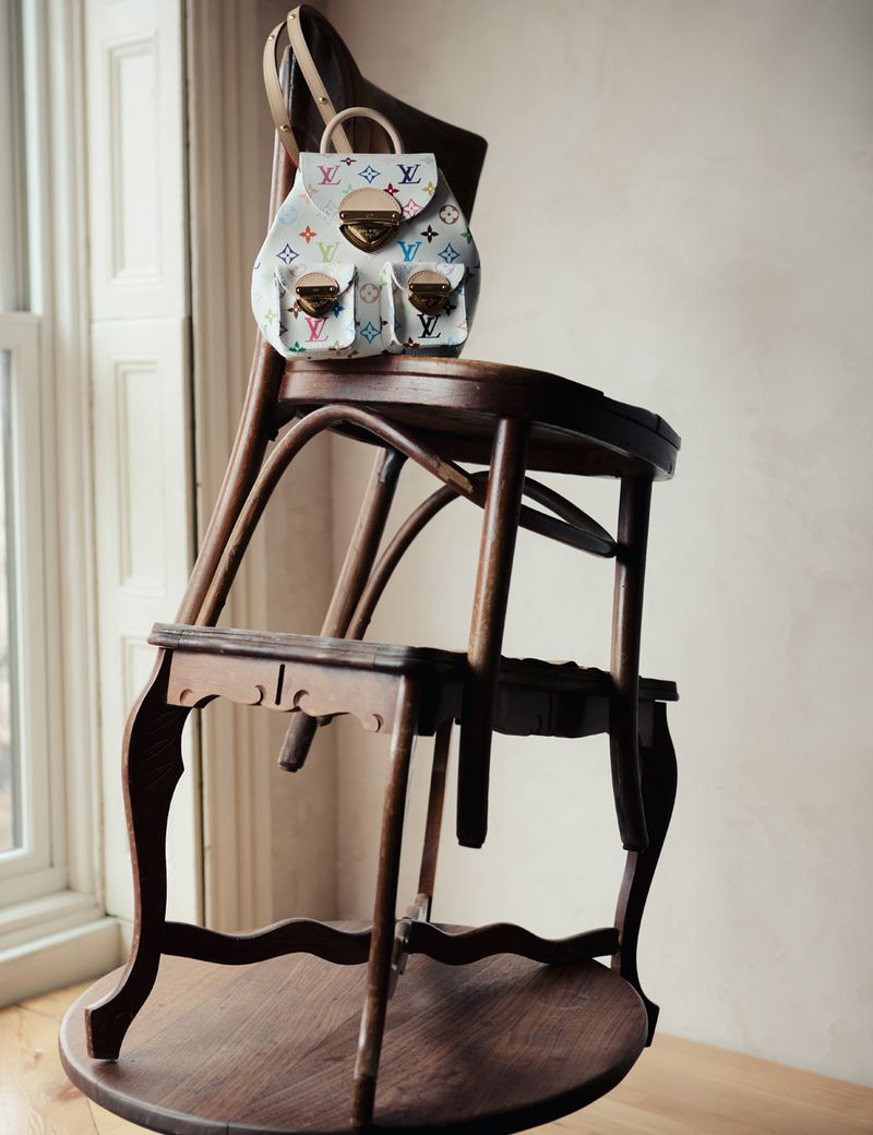 Louis Vuitton backpack perched atop an antique wooden chair near a window, showcasing luxury fashion with natural light.