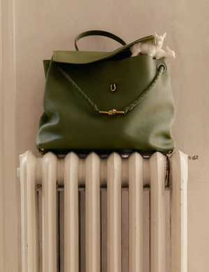 Olive green leather handbag resting on a white cast-iron radiator with small white animal figurines peeking out.