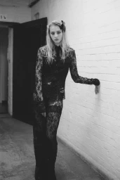 Model Annie Arnander wearing black lace clothing leaning against a white brick wall in a corridor