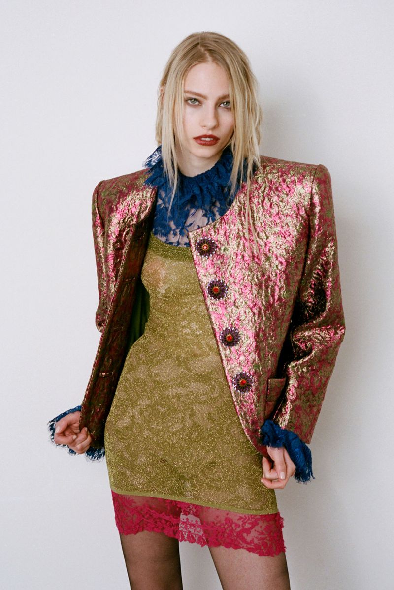 Model Annie Arnander wearing a textured metallic jacket and gold dress against a white seamless background