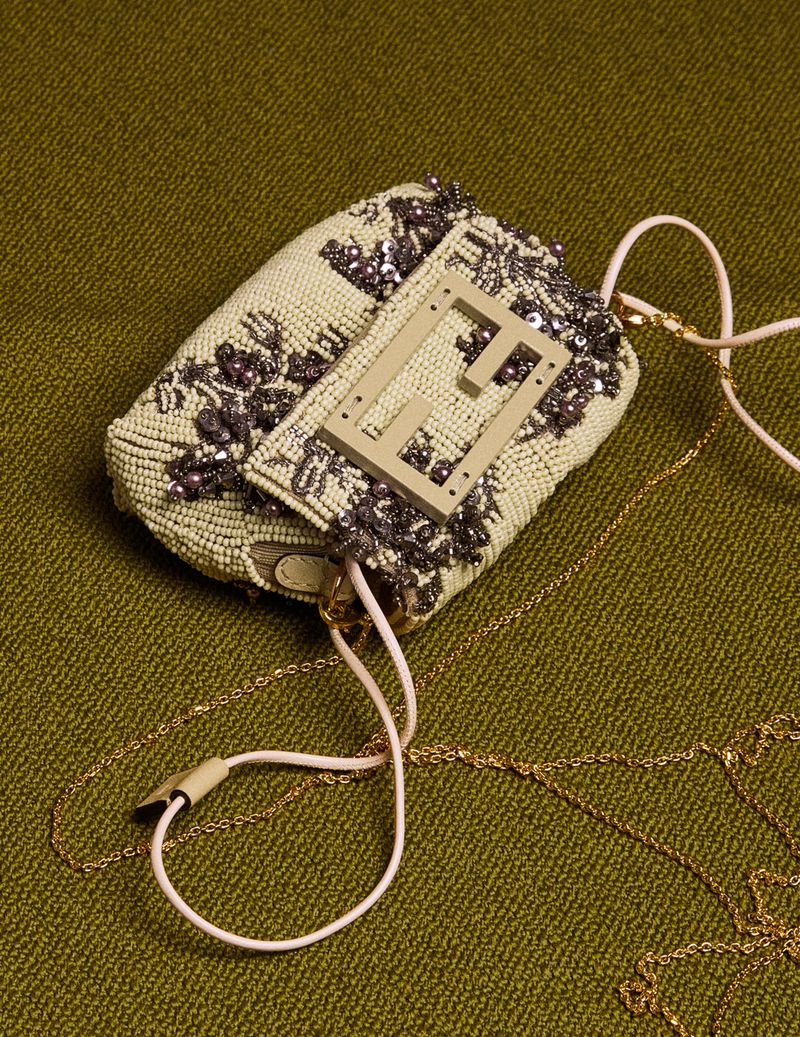 Beaded Fendi Baguette with floral embellishments and gold chain strap on olive green textured surface, top-down studio shot.
