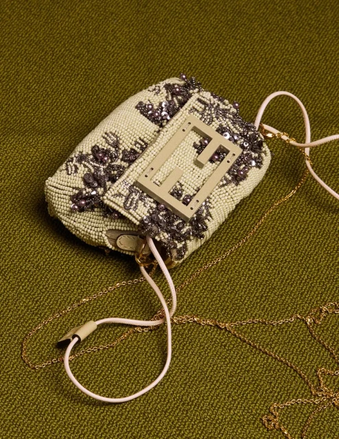 Beaded Fendi Baguette with floral embellishments and gold chain strap on olive green textured surface, top-down studio shot.