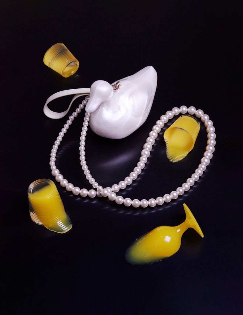 Elegant composition featuring a white swan purse, pearl necklace, and translucent yellow heels on a glossy black surface.