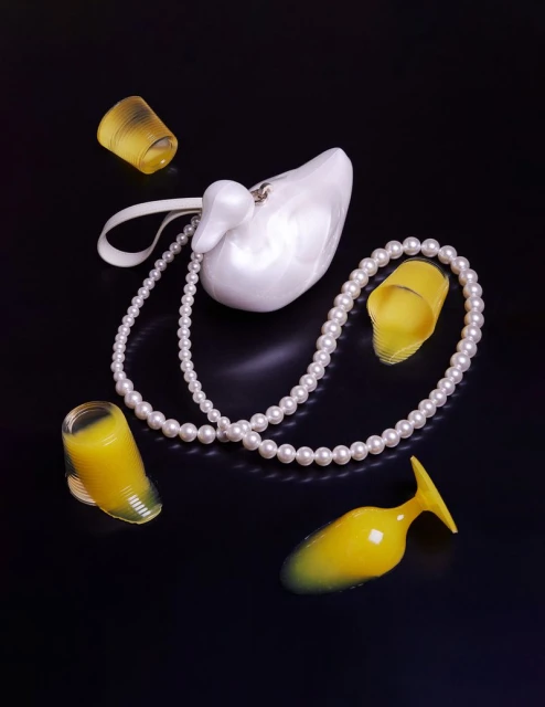 Elegant composition featuring a white swan purse, pearl necklace, and translucent yellow heels on a glossy black surface.