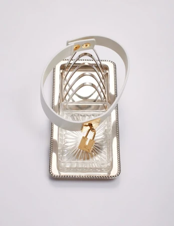 Silver plated toast rack with a white leather dog collar with gold padlock on a white background in a studio setting.
