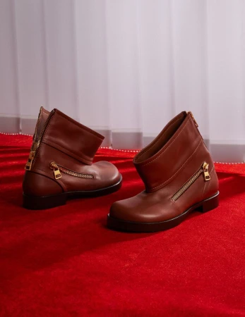 Two brown leather ankle boots with zipper details on a red carpet in a photo studio with soft window light creating a fashion product shot.