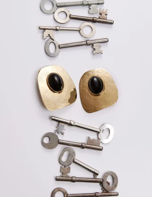 A pair of gold earrings with black stones arranged vertically alongside multiple silver antique keys on a light grey background.
