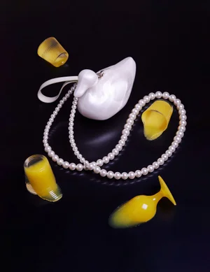 White duck shaped handbag with a pearl necklace and yellow liquid cups on black